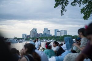 People gather by water, viewing a distant city skyline