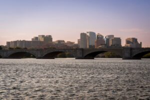 View of Arlington Memorial Bridge with modern skyline and calm river under twilight sky.