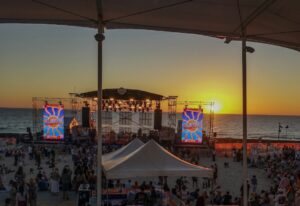 A crowd on a beach at a music festival during the golden hour